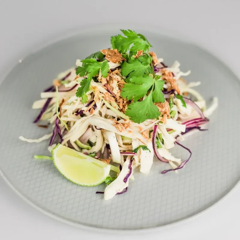 Plated salad of shredded cabbage, protein, cilantro, crispy bits, lime.