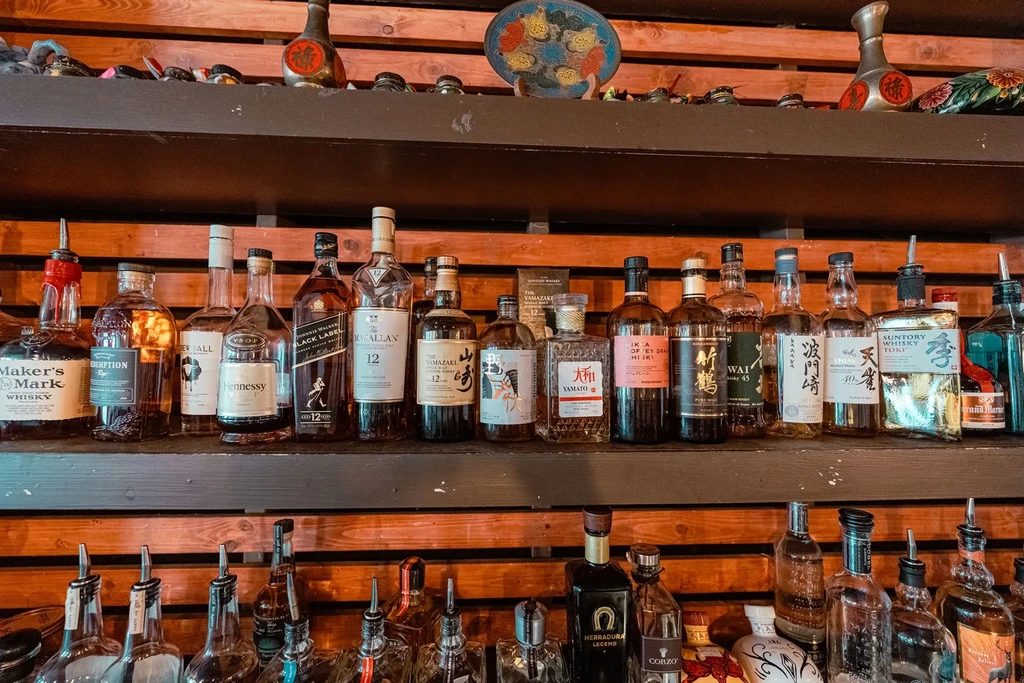 Assortment of whiskies and spirits on dark wooden bar shelves with decor.