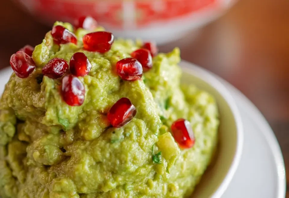 Chunky green guacamole topped with bright red pomegranate seeds in a bowl.