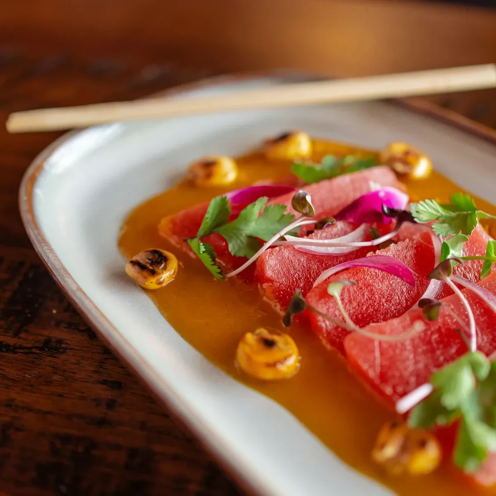 Plated deep red slices, golden sauce, corn, herbs, red onion, chopsticks.