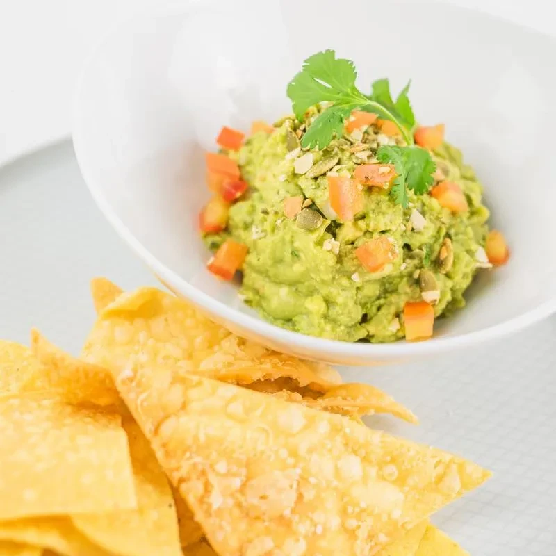Guacamole bowl with tomatoes, pepitas, cilantro, and tortilla chips.