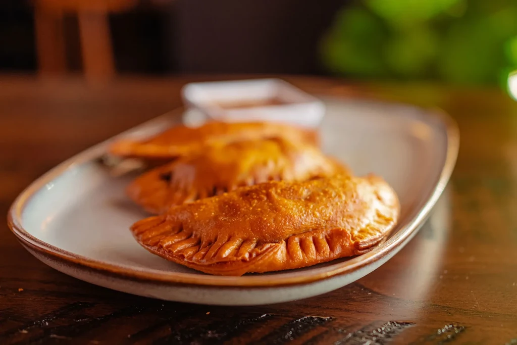 Three golden-brown fried pastries on an oval plate, sauce dish visible.