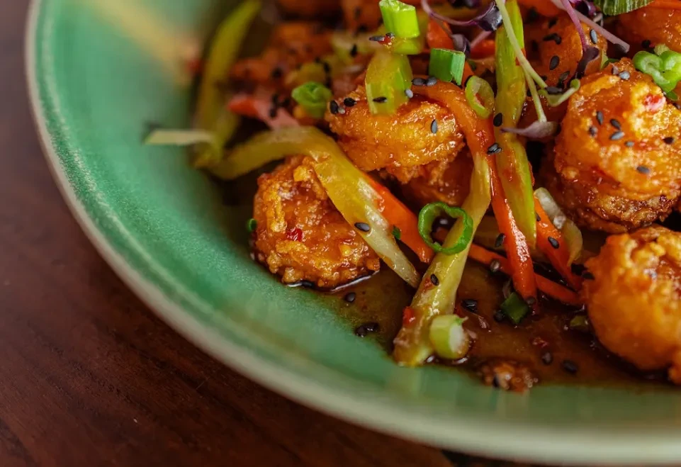 Golden fried food with reddish-orange sauce, vegetables, and sesame seeds.