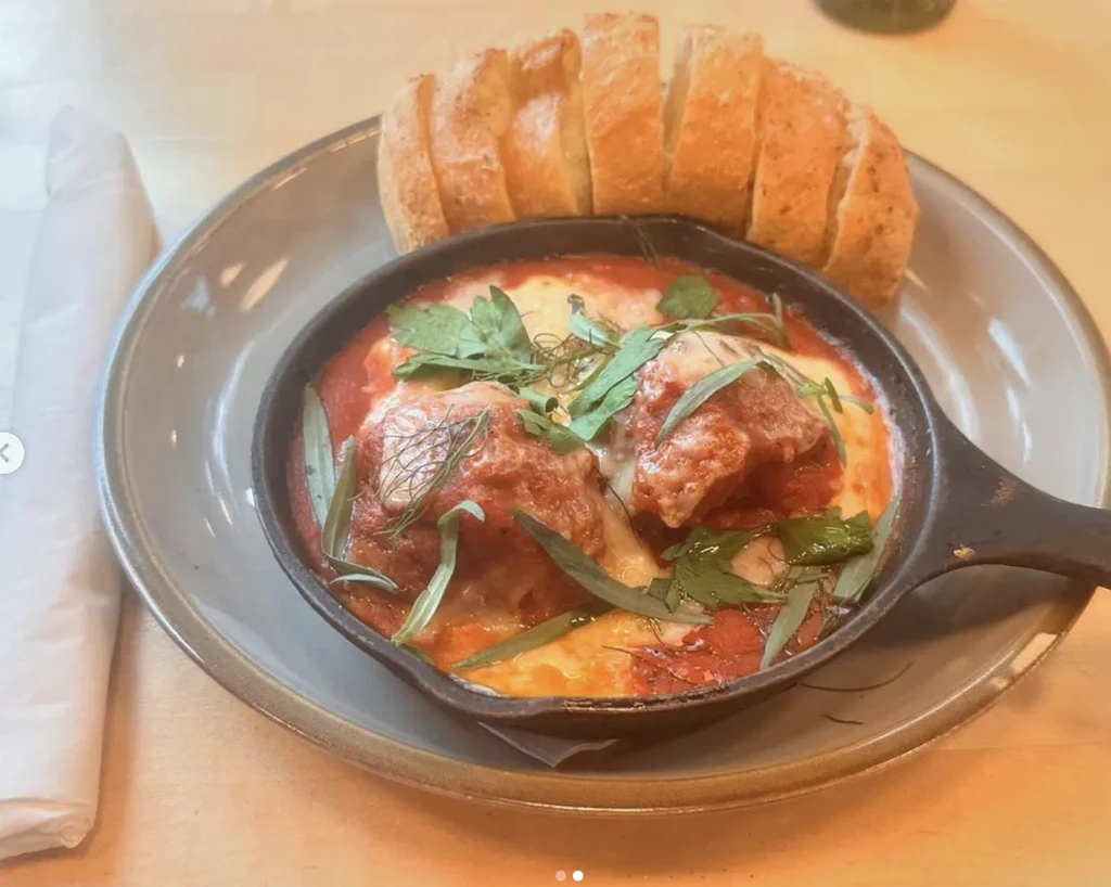 Cast iron pan of meatballs with cheese, herbs, and crusty bread.