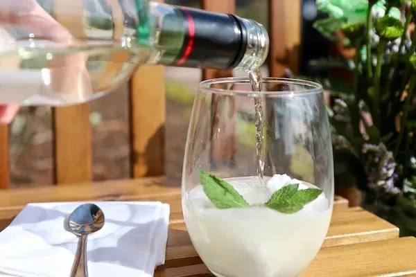 Liquid poured into a mint-garnished drink on a sunny day.