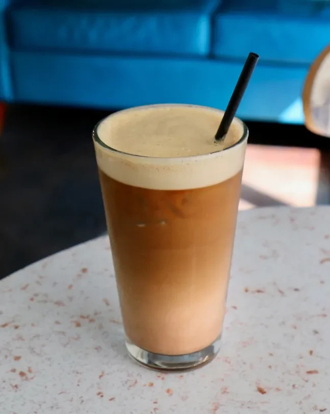 Layered beverage with creamy foam and black straw on speckled table.