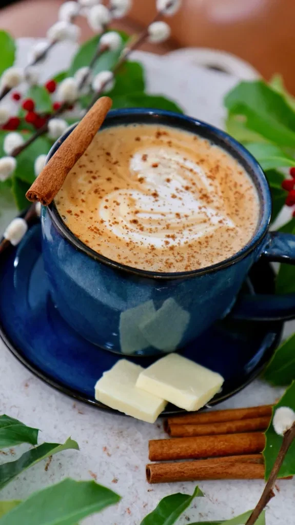 Dark blue mug with heart latte art, cinnamon, and white chocolate pieces.