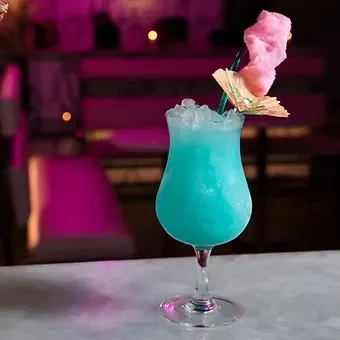 Aqua frozen cocktail with crushed ice, pink cotton candy, and umbrella.