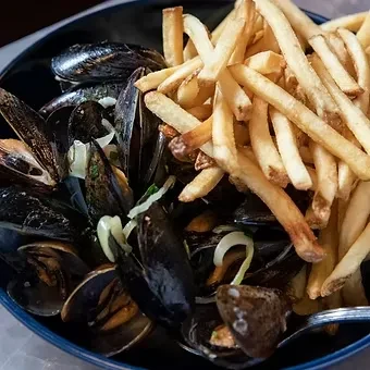 Mussels with onions and herbs, beside golden french fries in a bowl.