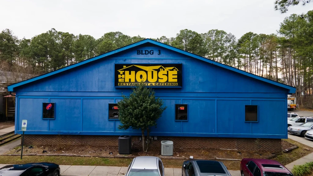 Blue "THE HOUSE" restaurant building with yellow sign and parked cars.