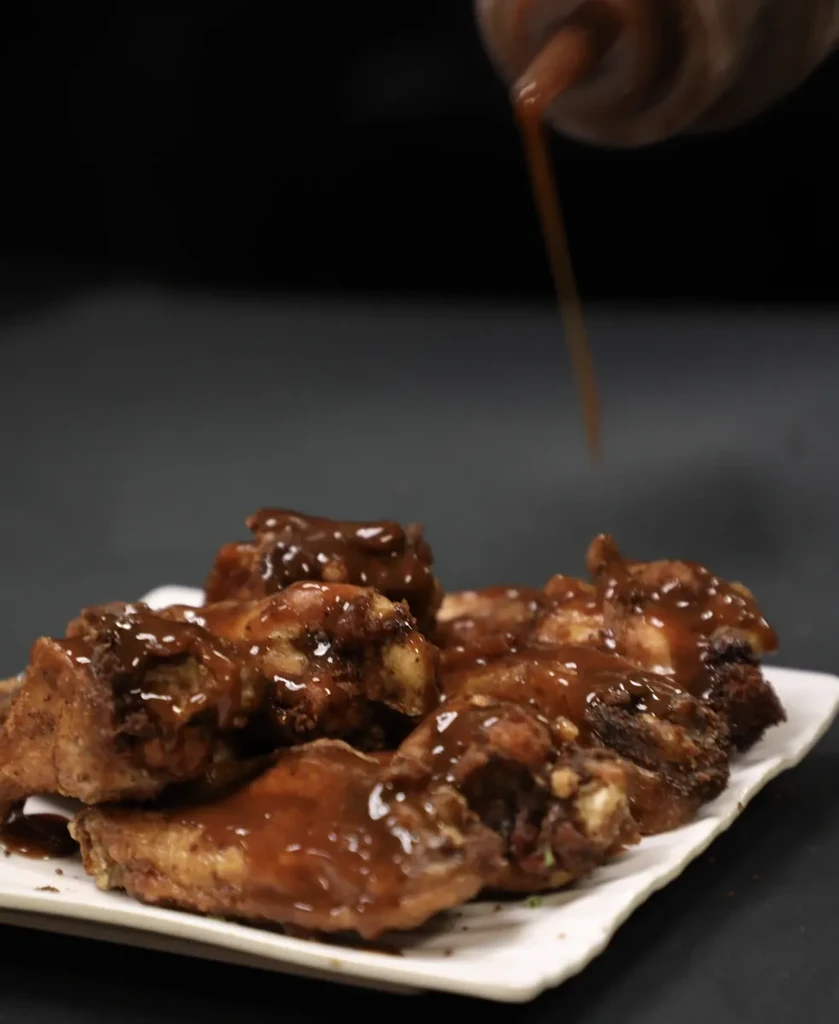 Close-up: Hand pouring dark sauce over glistening chicken wings.