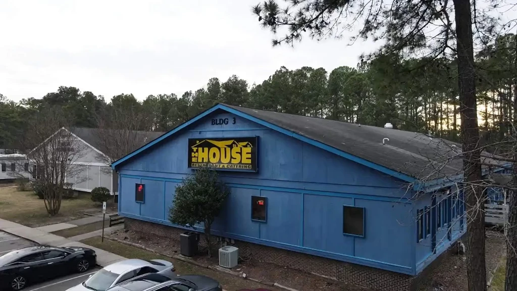 Blue restaurant building with "THE HOUSE" sign and parked cars.