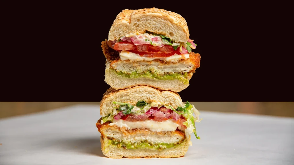 Stacked sandwich with breaded cutlet, cheese, tomatoes, and greens.