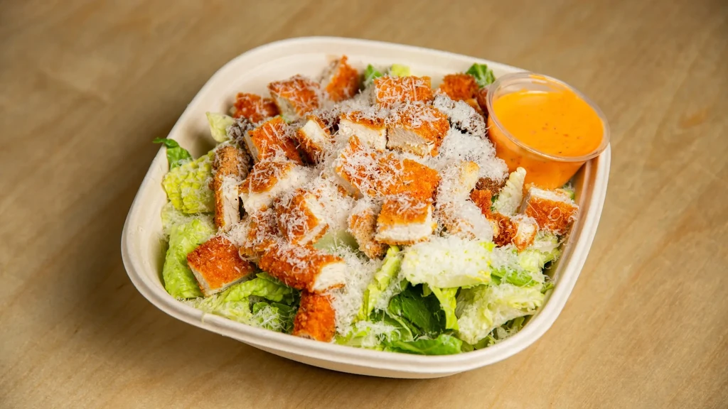 Fried chicken salad with lettuce, cheese, and dressing in takeout container.