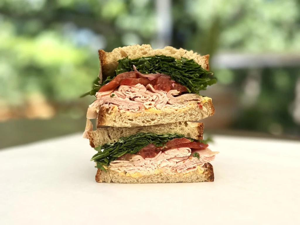 Cut-in-half stacked deli meat sandwich with greens and tomato.
