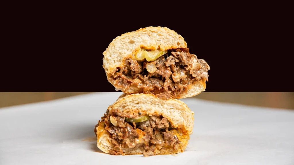 Stacked cheesesteak sandwich halves with abundant meat, cheese, onions, peppers.