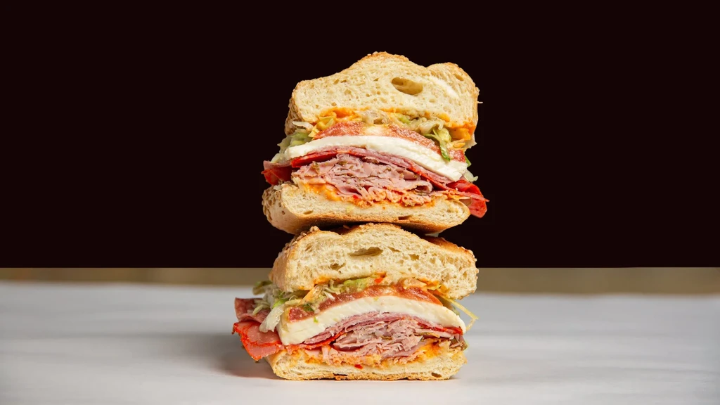 Large, stacked deli sandwich with meat, mozzarella, lettuce, sesame roll.