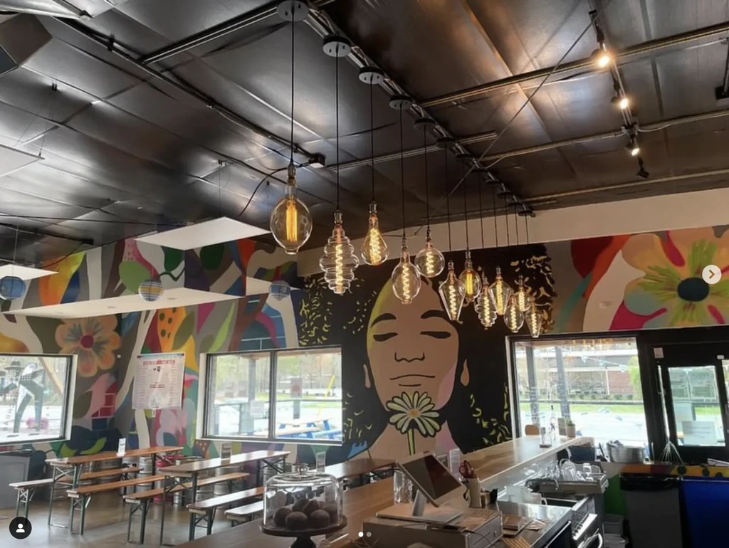 Vibrant restaurant interior with colorful murals, Edison bulbs, and a wooden bar.