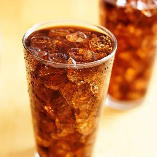 Two glasses of bubbly cola with ice and condensation.