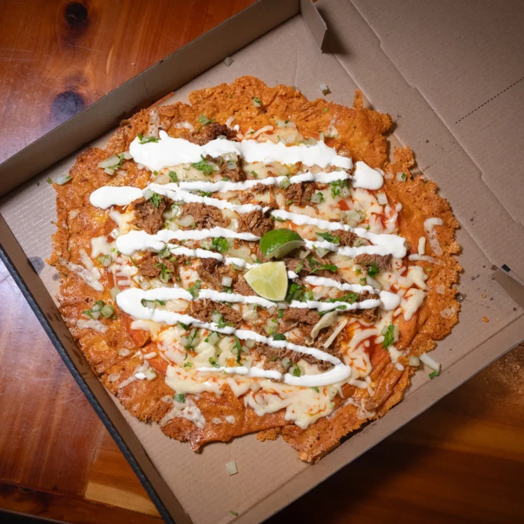 Crispy meat and cheese flatbread with lime wedges in a takeout box.