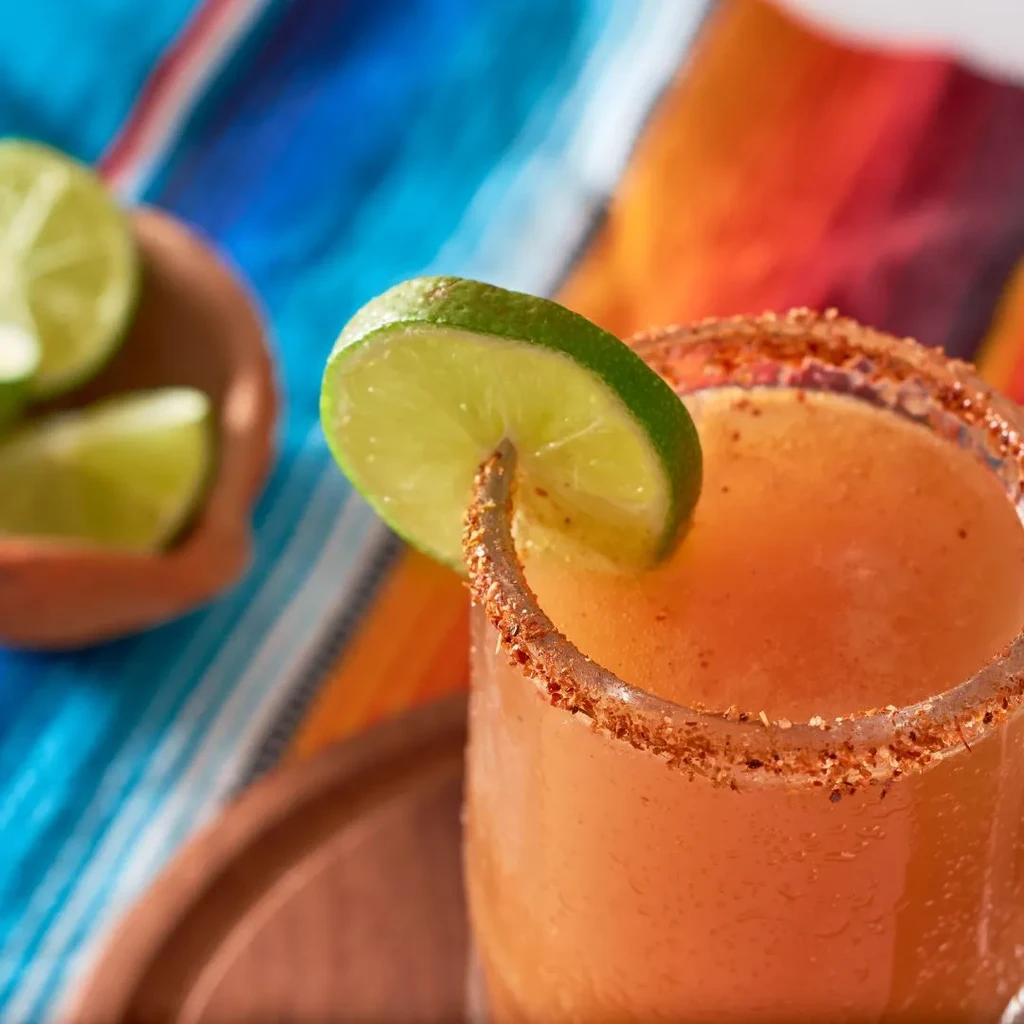 Orange drink with chili-lime rim and lime slice on a serape.