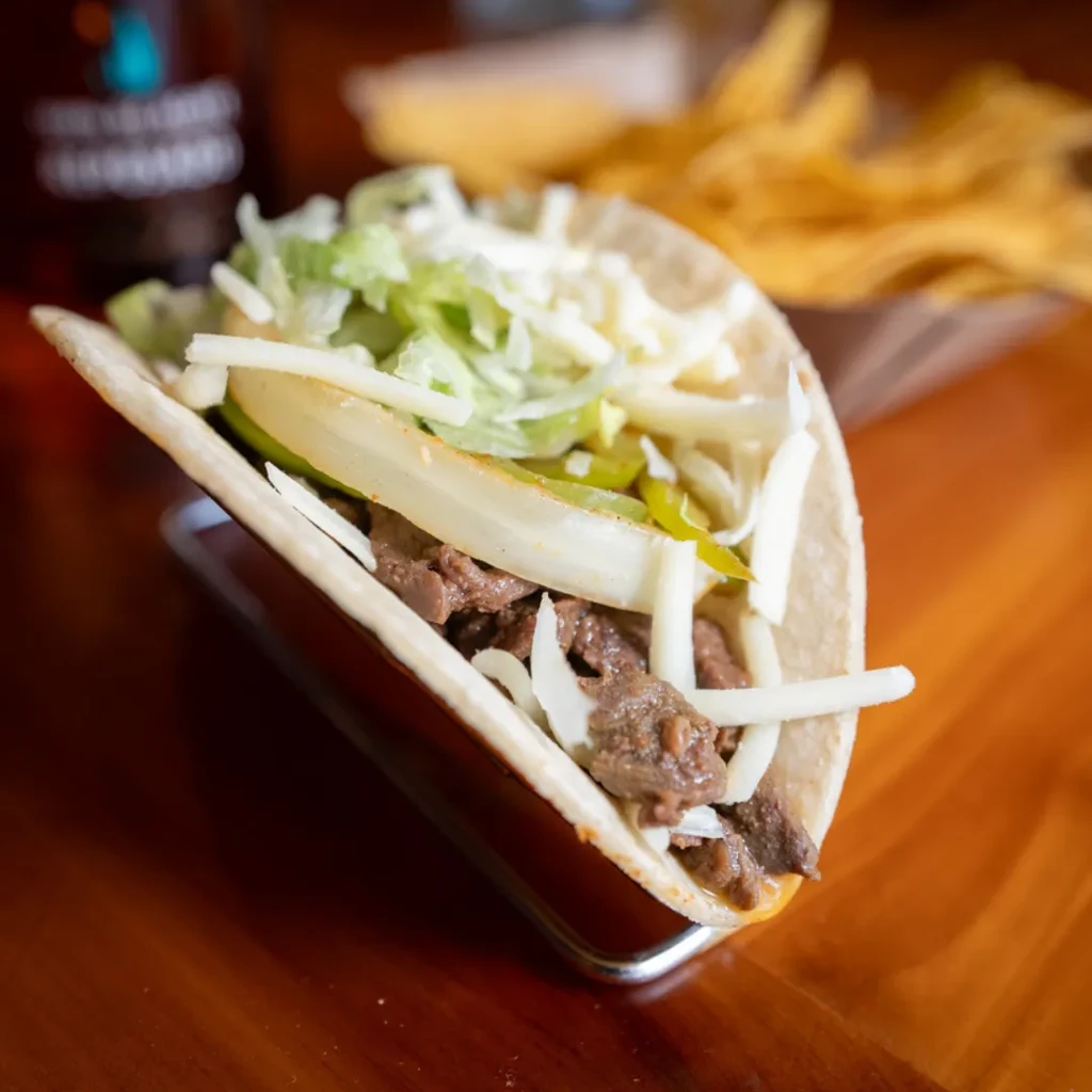 Single soft taco with shredded meat, cheese, lettuce, and onion.
