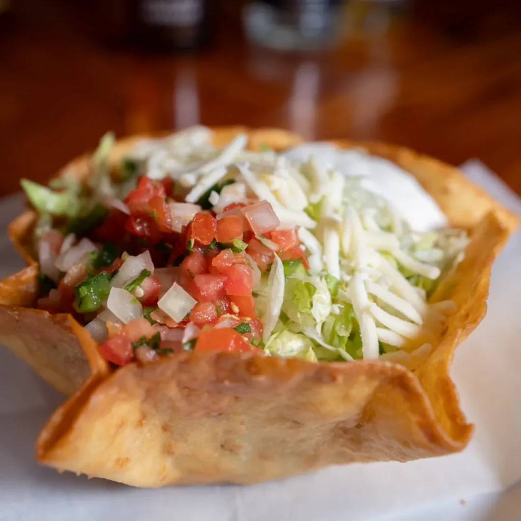 Taco salad in fried bowl with pico de gallo, lettuce, cheese, sour cream.