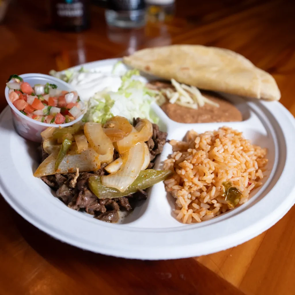 Sectioned plate of Mexican steak, rice, beans, tortilla, pico, and crema.