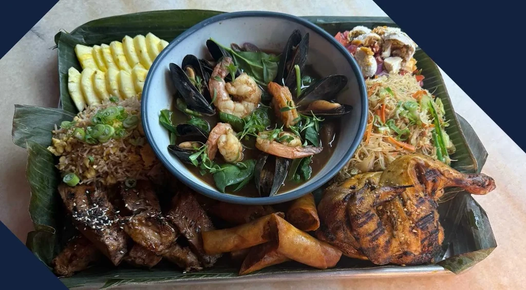 Feast platter of seafood, grilled meats, rice, noodles, and spring rolls.