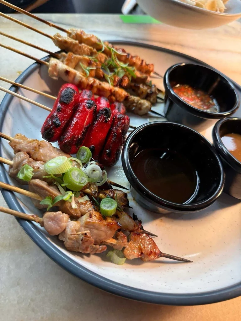 Grilled meat and sausage skewers garnished with green onions and three sauces.