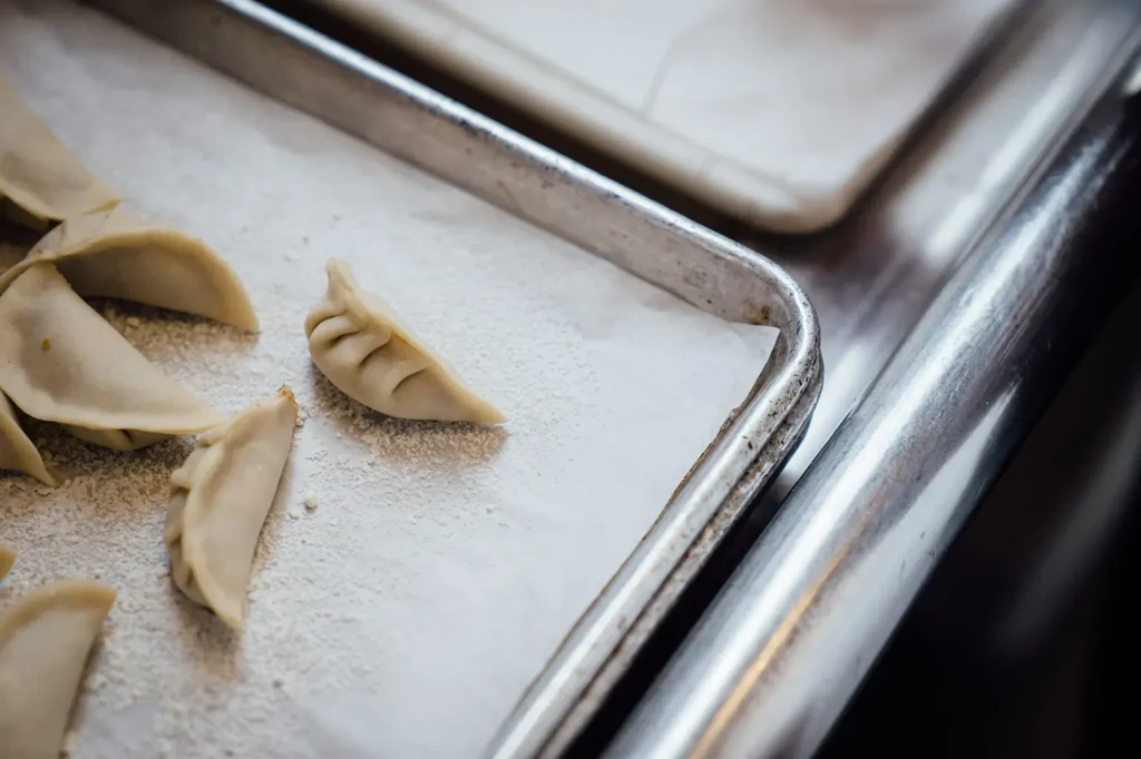 Several raw, crimped dumplings on parchment in a metal tray.