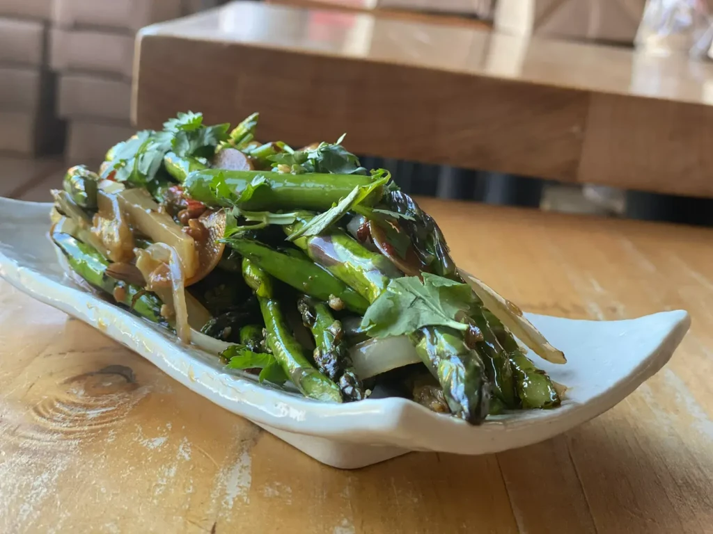 Asparagus, onions, and cilantro stir-fry on a white rectangular plate.