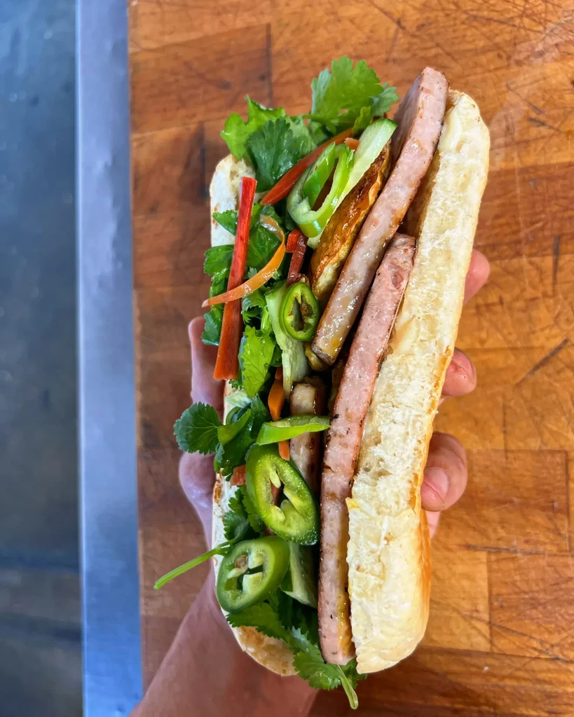 Crispy Banh Mi sandwich with pork, cilantro, pickled vegetables held by hand.