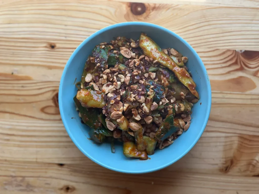 Overhead: Turquoise bowl of sauced cucumber and chopped nuts.