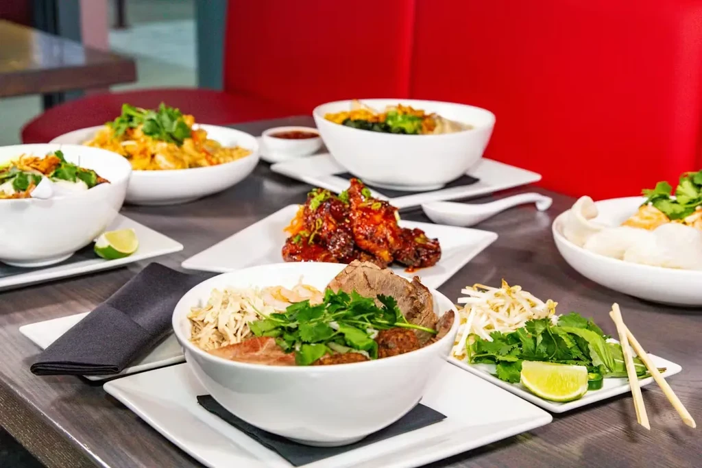 Various Asian dishes including pho and glazed chicken on a restaurant table.