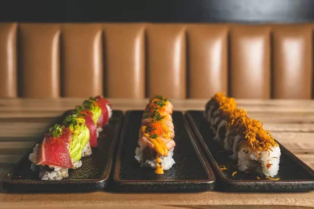 Three varied sushi rolls on black plates in a restaurant.