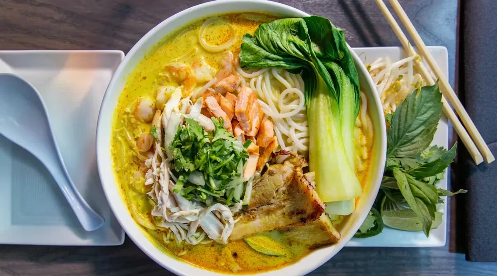 Top-down, colorful Asian noodle soup with proteins and fresh garnishes.