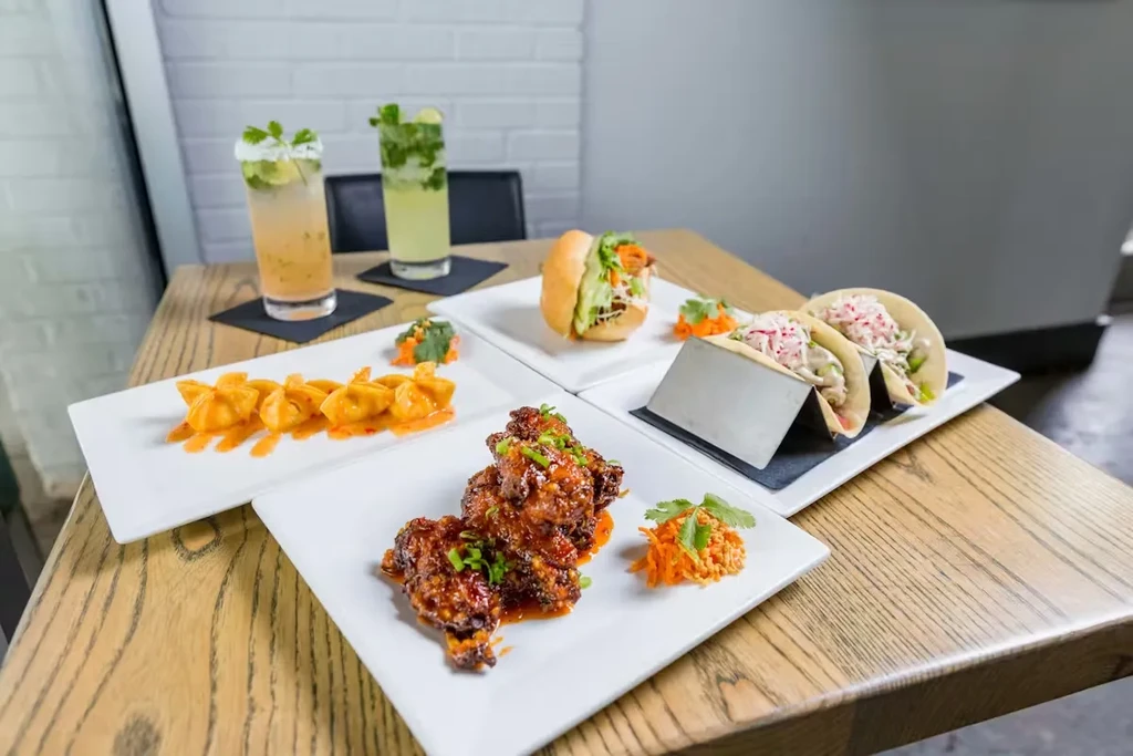 Fried dumplings, chicken wings, tacos, slider, and cocktails on a table.