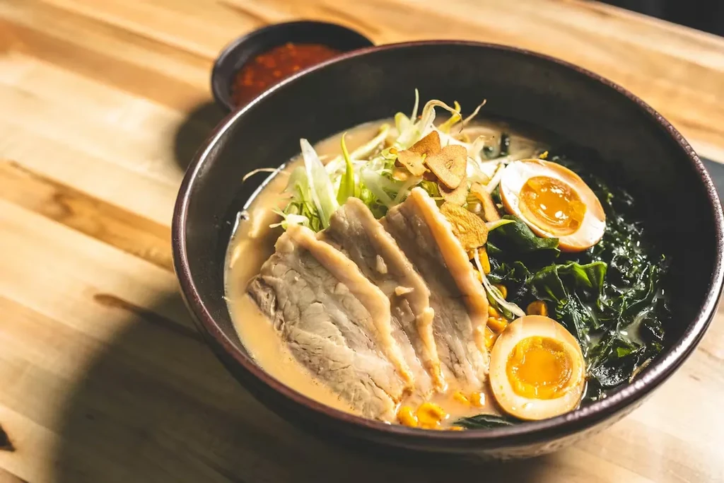 High-angle ramen bowl with pork belly, egg, and fresh vegetables.