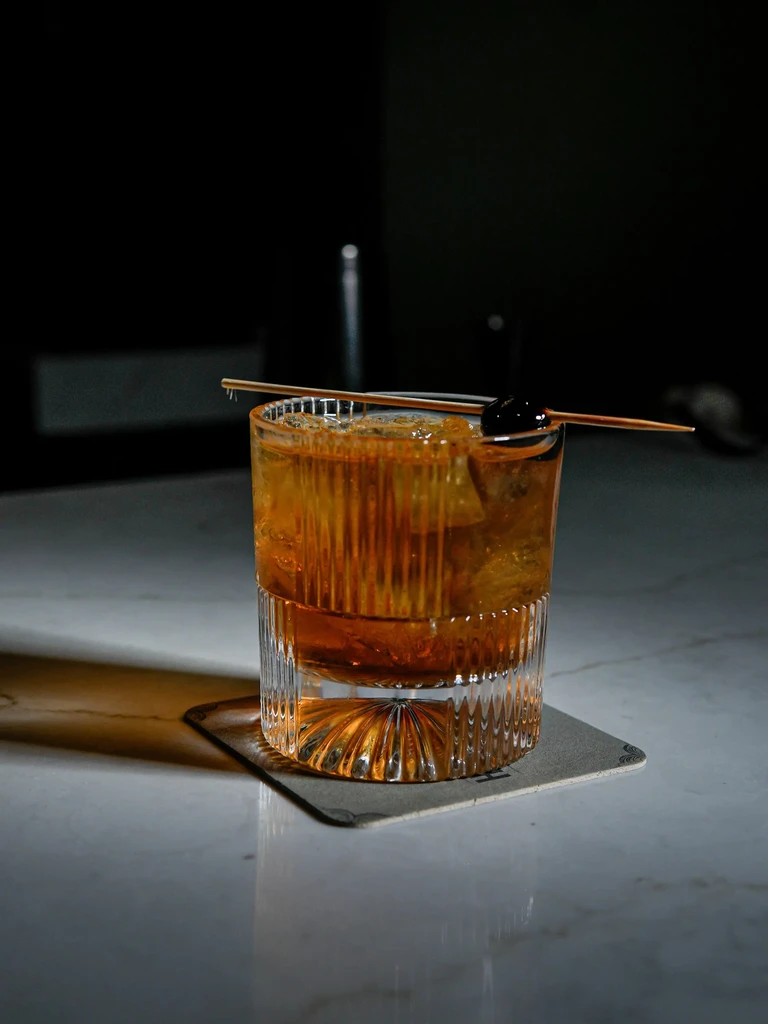 An Old Fashioned cocktail in a rocks glass with a cherry garnish.