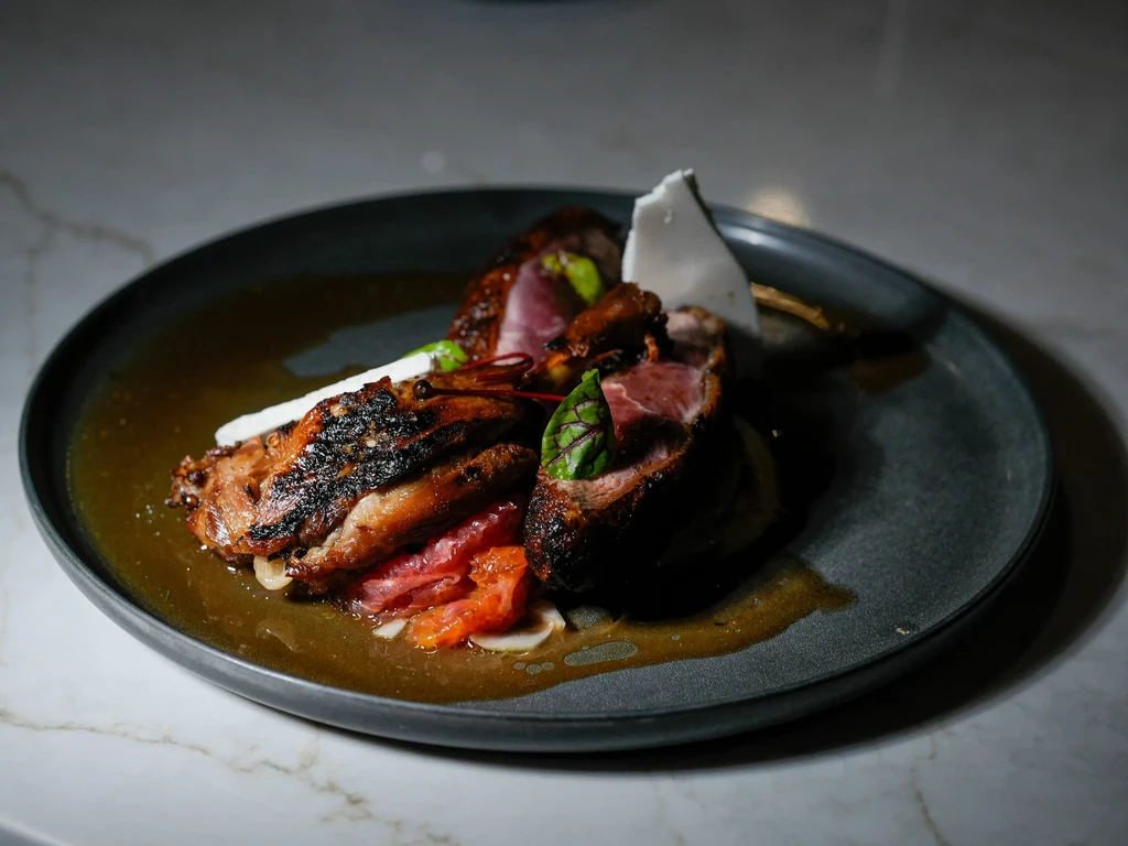 Grilled meat with sauce, garnished with herbs and citrus, on a black plate.