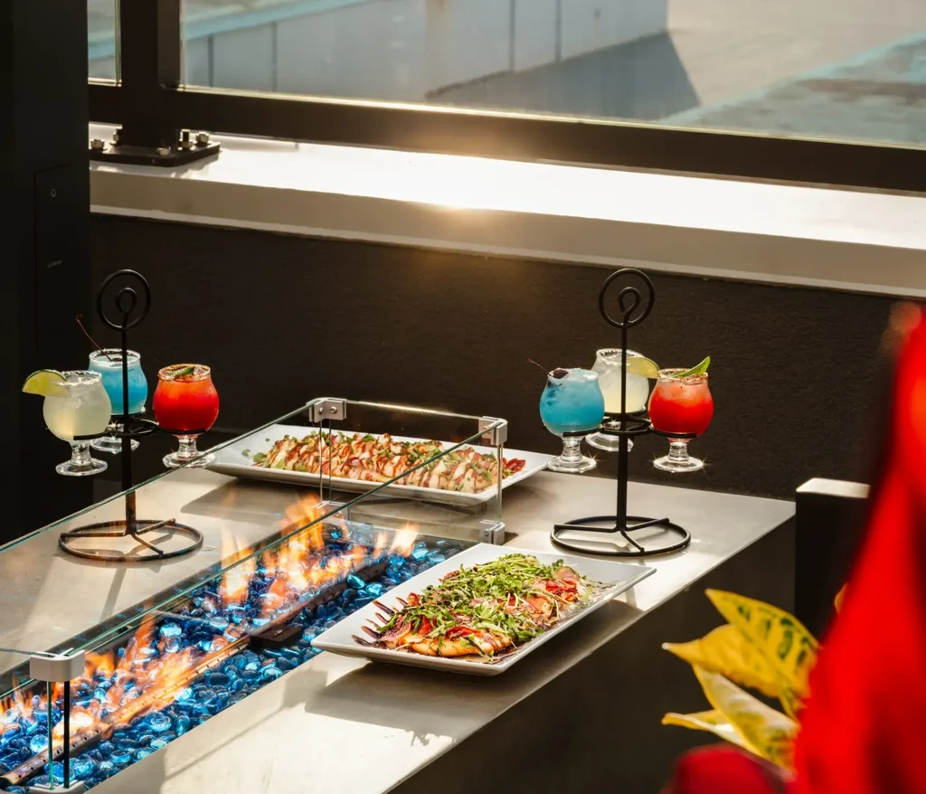 Modern table with blue fire, appetizers, and six vibrant cocktails.
