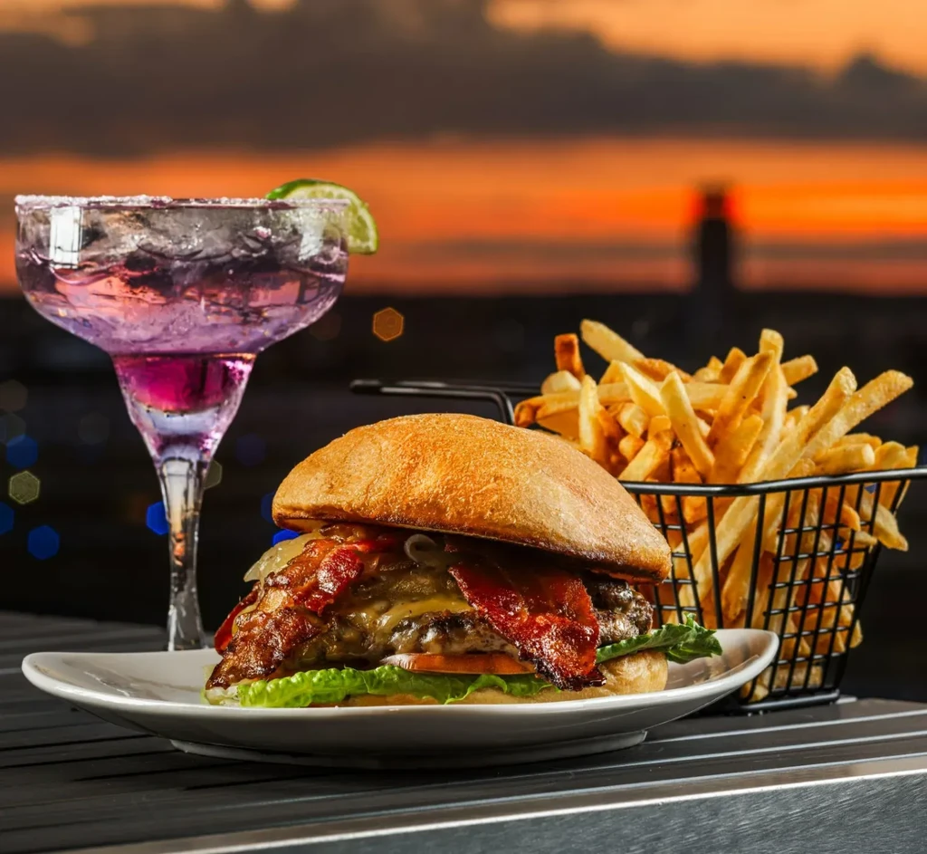 Gourmet burger, fries, and purple cocktail at sunset.