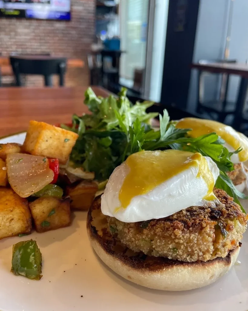 A plate of eggs benedict with potatoes and salad on a table.