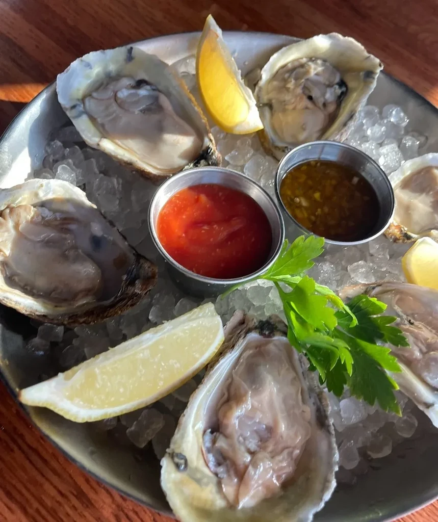 A plate of oysters on ice with lemon, cocktail sauce, and mignonette.