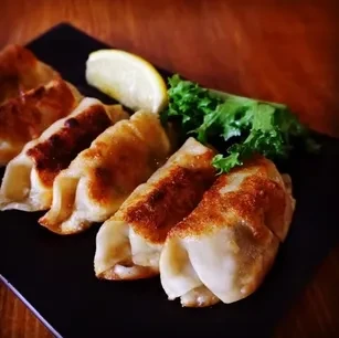 Pan-fried gyoza with a lemon slice and lettuce on a black plate.