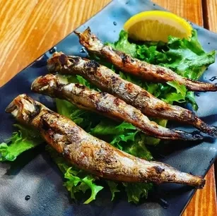 Four grilled fish, capelin or shishamo, on lettuce with a lemon slice.