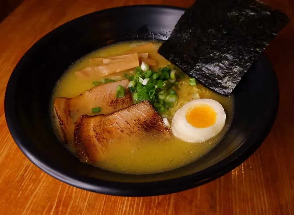 A black bowl of ramen with pork, egg, seaweed, and scallions.