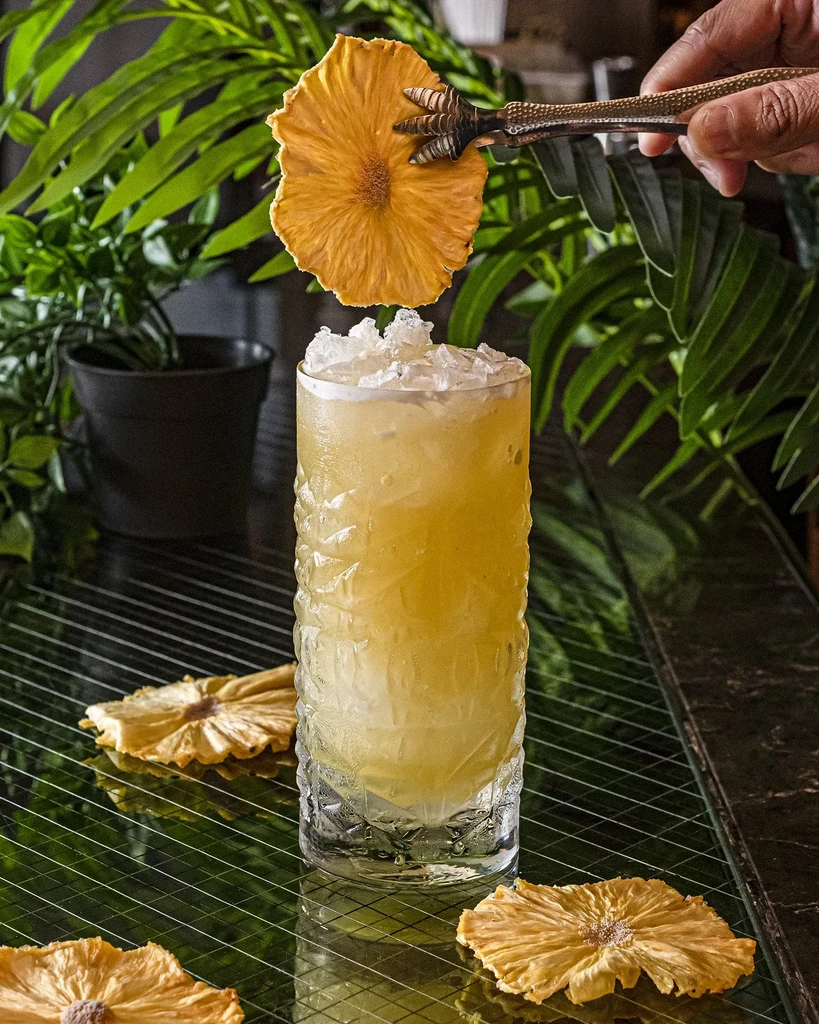 A hand garnishes a crushed ice drink with a dried pineapple slice.