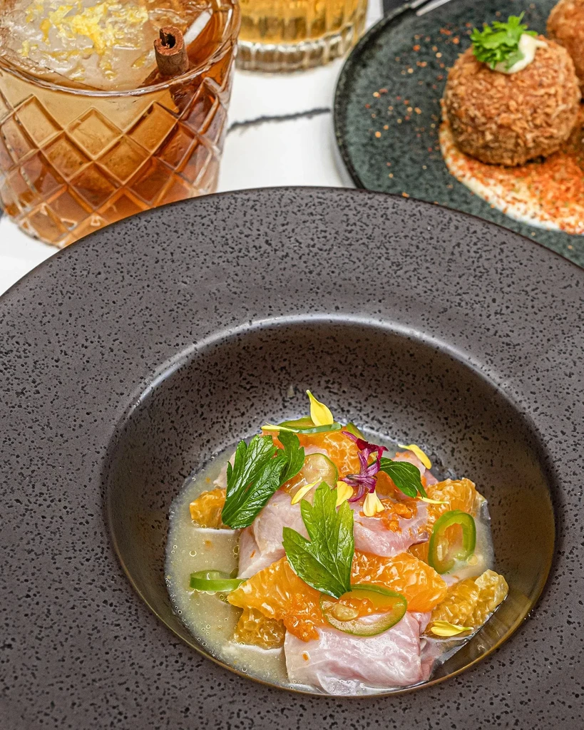 Ceviche with orange, mint, and jalapeños in a black bowl.